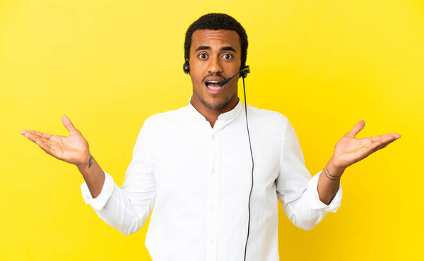 African American Telemarketer man working with a headset over isolated yellow background with shocked facial expression