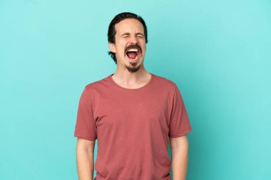 Kafkasyalı genç adam mavi arka planda izole edilmiş ve ağzı açık bağırıyor.