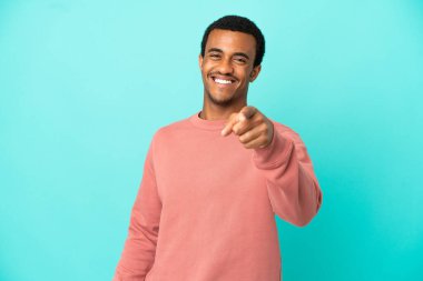 İzole edilmiş mavi arka planda Afro-Amerikalı yakışıklı adam mutlu bir ifadeyle öne bakıyor.