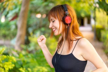 Genç, güzel, kızıl saçlı, açık havada müzik dinleyip dans eden bir kadın.
