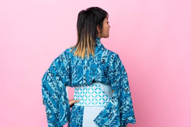 Kimono giyen genç bir kadın, mavi arka planda izole edilmiş arka planda ve yan bakıyor.