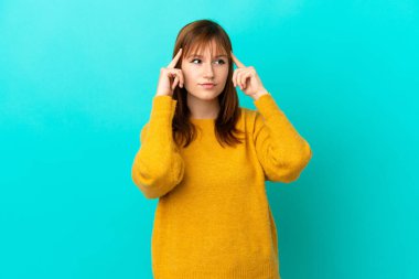 Kızıl saçlı kız mavi arka planda izole edilmiş. Şüpheleri ve düşünceleri var.