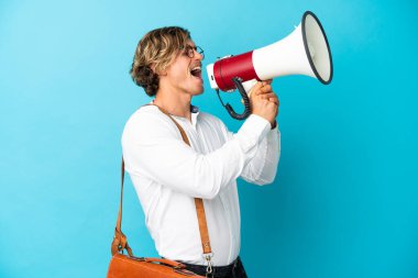 Sarışın genç işadamı mavi arka planda izole edilmiş megafonla bağırıyor.