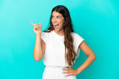 Kafkasyalı genç kadın mavi arka planda izole edildi. Çözümün farkına varmak için parmağını kaldırdı.