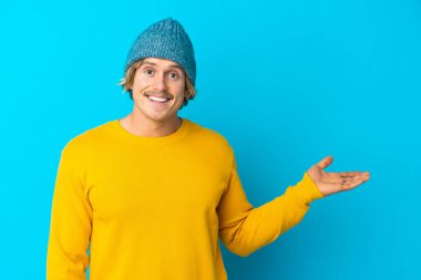 Mavi arka planda izole edilmiş yakışıklı sarışın bir adam. Avucunun içinde reklam koymak için hayali bir alan tutuyor.