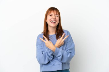 Kızıl saçlı kız beyaz arka planda izole edilmiş gülümsüyor ve zafer işareti gösteriyor.