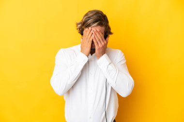 Tele pazarlamacı adam kulaklıkla çalışıyor. Sarı arka planda, yorgun ve hasta bir ifadeyle izole edilmiş.