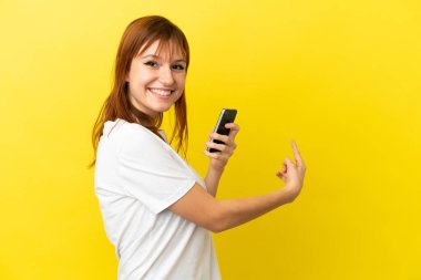 Kızıl saçlı kız sarı arka planda cep telefonu kullanarak izole edilmiş.