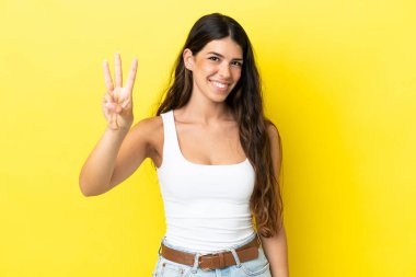 Sarı arka planda izole edilmiş beyaz kadın mutlu ve parmaklarıyla üçe kadar sayıyor.