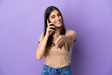 Mor arka planda izole edilmiş cep telefonu kullanan beyaz bir kadın iyi bir anlaşma için el sıkışıyor.