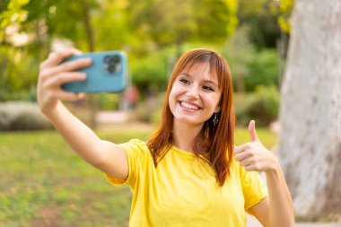 Dışarıdaki güzel kızıl saçlı kadın cep telefonuyla selfie çekiyor.