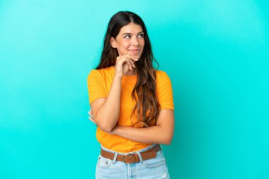 Kafkasyalı genç bir kadın mavi arka planda izole edilmiş bir şekilde yukarı bakarken bir fikir düşünüyor.