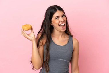 Pembe arka planda izole edilmiş beyaz bir kadın elinde mutlu bir ifadeyle donut tutuyor.