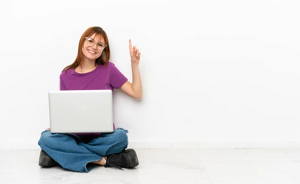 Rothaarige Mädchen Mit Einem Laptop Auf Dem Boden Sitzend Zeigt — Stockfoto