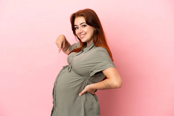 Młoda Ruda Biała Kobieta Odizolowana Różowym Tle Ciąży Wskazując Brzuch — Zdjęcie stockowe