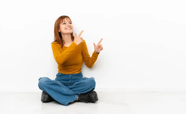 Roodharige Meisje Zitten Vloer Geïsoleerd Witte Achtergrond Wijzend Met Wijsvinger — Stockfoto