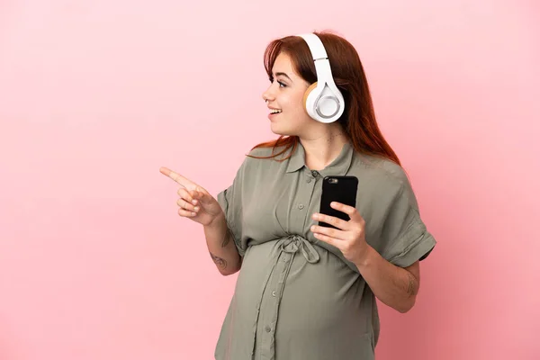 Νεαρή Κοκκινομάλλα Καυκάσια Γυναίκα Απομονωμένη Ροζ Φόντο Έγκυος Και Ακούγοντας — Φωτογραφία Αρχείου