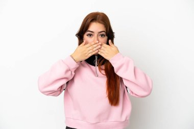 Beyaz arka planda izole edilmiş genç, kızıl saçlı bir kadın elleriyle ağzını kapatıyor.