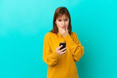 Kızıl saçlı kız mavi arka planda izole edilmiş düşünüyor ve mesaj gönderiyor.