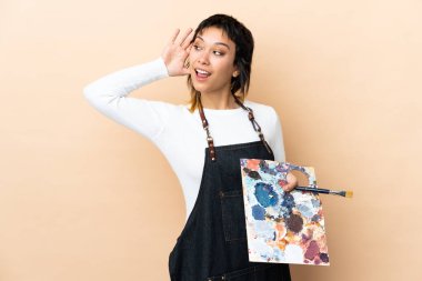 Genç sanatçı arka planda bir palet tutuyor ve bir şeyler dinliyor.