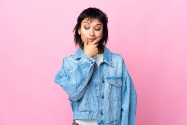 Genç Uruguaylı kadın pembe arka planda kuşkuları ve şaşkın bir yüz ifadesi var.