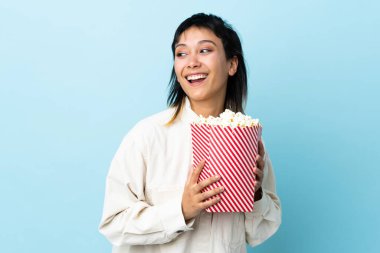 Genç Uruguaylı kadın izole edilmiş mavi arka planda elinde koca bir kova patlamış mısır tutuyor.