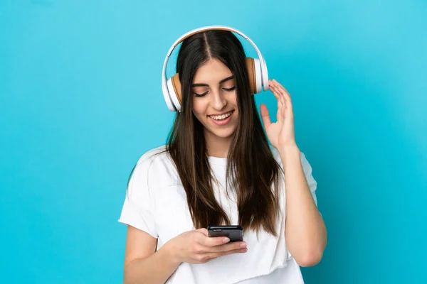 Jovem Caucasiana Isolada Fundo Azul Ouvindo Música Olhando Para Celular — Fotografia de Stock