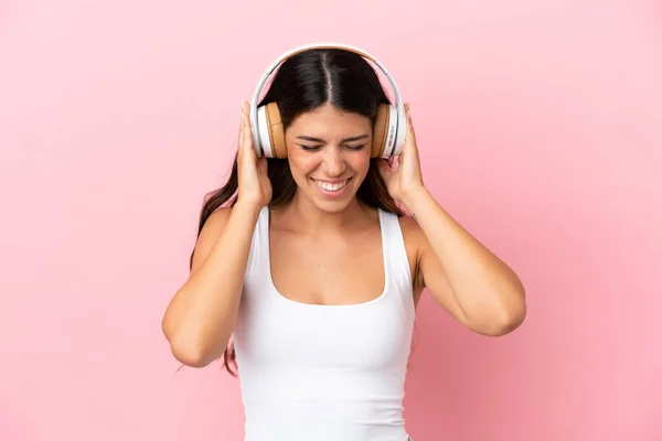 若いですCaucasian女性隔離上のピンクの背景リスニング音楽 — ストック写真