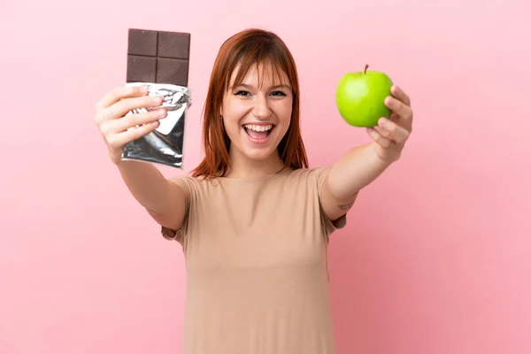 Roodharige Meisje Geïsoleerd Roze Achtergrond Nemen Van Een Chocolade Tablet — Stockfoto