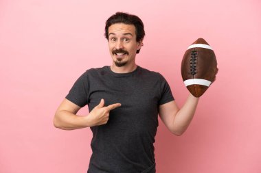Genç beyaz adam rugby oynuyor. Pembe arka planda izole edilmiş ve yüzünde sürpriz bir ifade var.