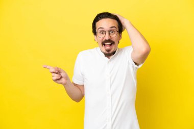 Sarı arka planda izole edilmiş genç beyaz adam şaşırdı ve parmağını yana çevirdi.