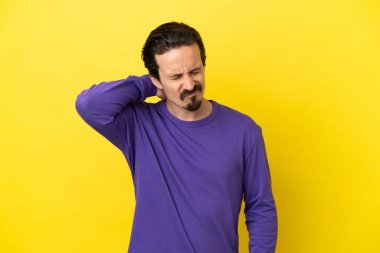 Sarı arka planda boynu ağrıyan genç, beyaz bir adam.