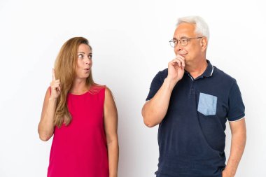 Orta yaşlı çift beyaz arka planda izole edilmiş bir şekilde ayakta duruyor ve bir fikir düşünüyorlar.