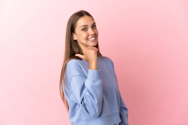 Soyutlanmış pembe arka planı olan genç bir kadın bir ürünü sunmak için kenarı işaret ediyor.