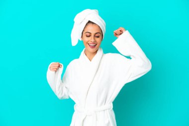 İzole edilmiş mavi arka planda bornozlu genç bir kadın zaferi kutluyor.