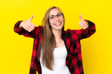 Sarı arka planda izole edilmiş genç bir İngiliz kadın baş parmak işareti yapıyor.
