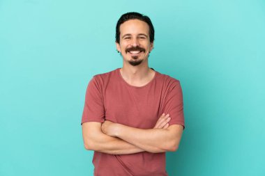 Mavi arka planda izole genç beyaz adam kollarını ön pozisyonda çapraz tutuyor.