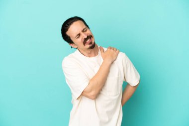 Genç beyaz adam mavi arka planda izole edildi. Omuz ağrısı çektiği için çabaladı.