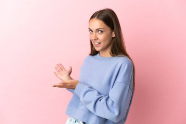 Soyutlanmış pembe arka planda genç bir kadın. Davet edilmek için ellerini yana uzatıyor.