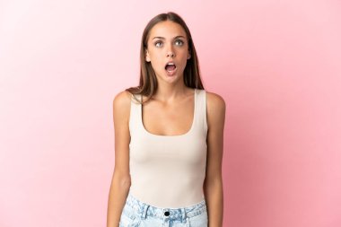 Soyutlanmış pembe arka planda genç bir kadın yukarı bakıyor ve şaşırmış bir ifadeyle