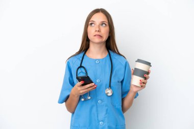 Genç cerrah doktor Litvanyalı kadın beyaz arka planda izole edildi. Elinde kahve ve bir şeyler düşünürken cep telefonu vardı.