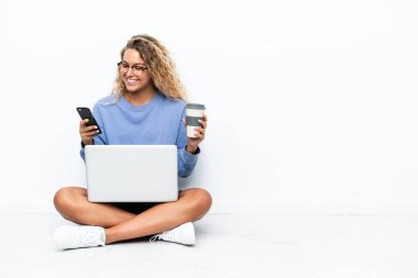 Kıvırcık saçlı, dizüstü bilgisayarı olan, elinde kahve ve cep telefonu olan bir kız.