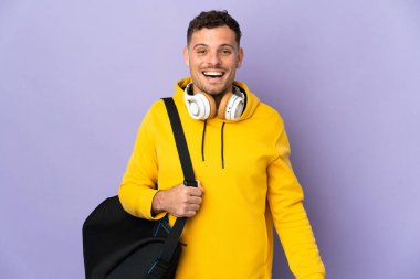 Çantası olan beyaz bir genç, mor bir arka planı ve şaşırtıcı bir yüz ifadesi var.