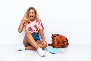 Genç bir bayan öğrenci yerde oturmuş, telefonla konuşuyor. Bana geri dönüş işareti ver.