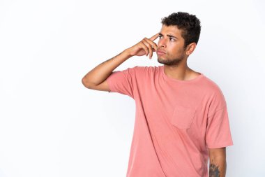 Genç ve yakışıklı Brezilyalı bir adam beyaz arka planda izole edilmiş. Delilik jesti yapıyor. Parmağını kafaya koyuyor.