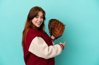 Beyzbol oynayan genç kızıl saçlı kadın mavi arka planda izole edilmiş.