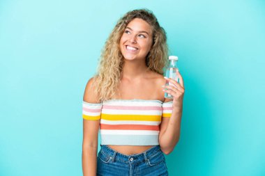 Mavi arka planda bir şişe suyu olan genç sarışın kadın yukarı bakarken bir fikir düşünüyor.