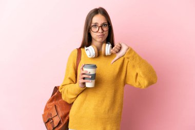 Soyutlanmış pembe arka planda genç bir bayan, olumsuz bir ifadeyle baş parmağını aşağı gösteriyor.