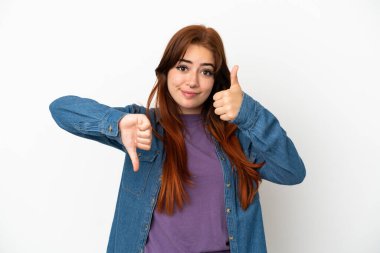 Genç kızıl saçlı kadın beyaz arka planda izole edilmiş, iyiye-kötüye işaret yapıyor. Evet ya da hayır arasında kararsız