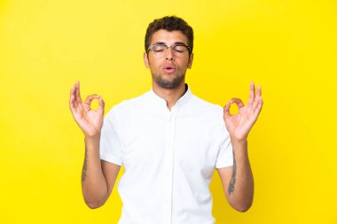Genç yakışıklı Brezilyalı adam, sarı arka planda izole edilmiş, zen pozisyonunda.